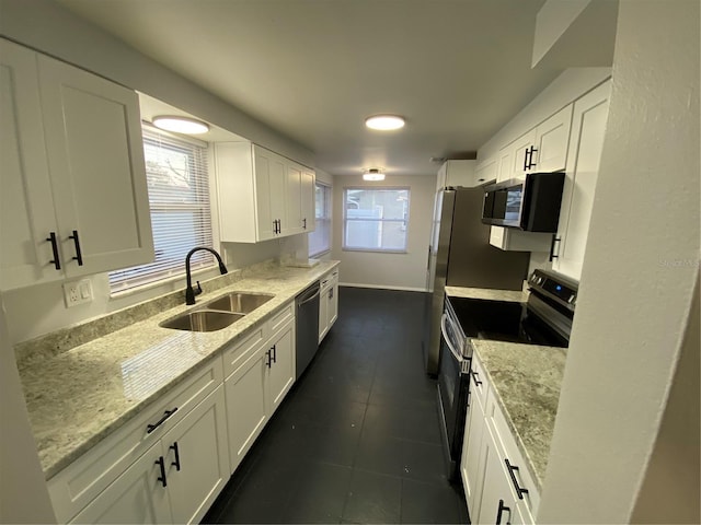 kitchen with appliances with stainless steel finishes, white cabinetry, sink, dark tile patterned flooring, and light stone counters