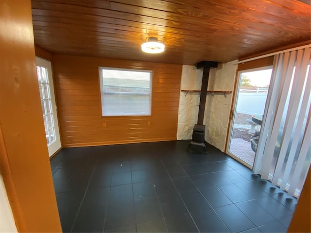 tiled empty room with a wood stove, wooden walls, and wood ceiling