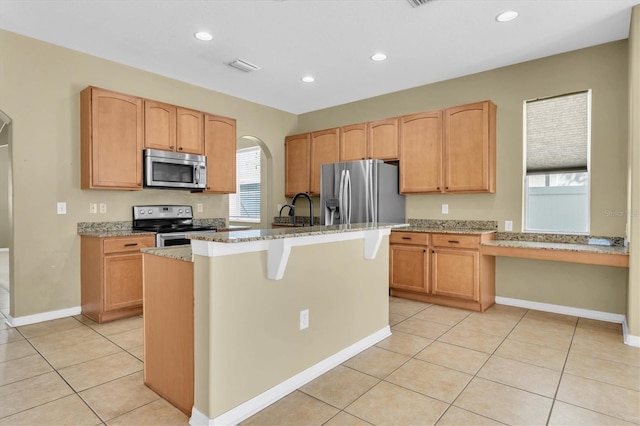 kitchen featuring light stone countertops, appliances with stainless steel finishes, a kitchen island with sink, and light tile patterned floors