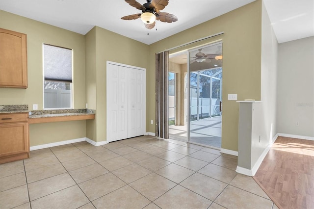 interior space with built in desk, ceiling fan, and light tile patterned flooring