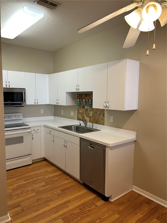 kitchen with appliances with stainless steel finishes, sink, hardwood / wood-style floors, and white cabinets