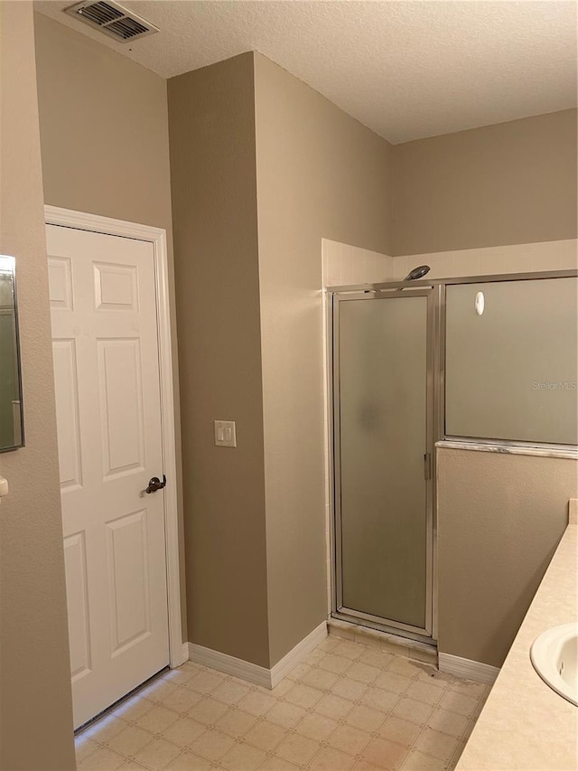 bathroom with vanity, a shower with shower door, and a textured ceiling