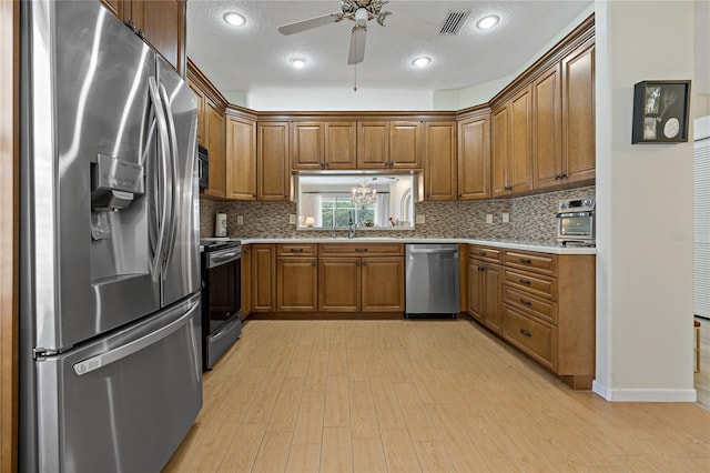 kitchen with a textured ceiling, ceiling fan, stainless steel appliances, light hardwood / wood-style floors, and decorative backsplash