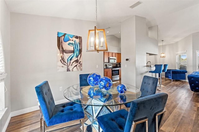 dining space featuring wood-type flooring, high vaulted ceiling, sink, and an inviting chandelier