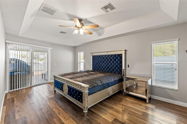 bedroom featuring multiple windows, access to exterior, dark hardwood / wood-style flooring, and a tray ceiling