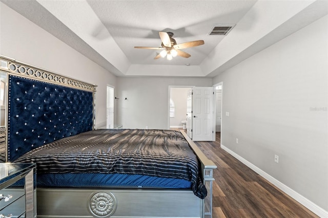 bedroom with connected bathroom, dark hardwood / wood-style flooring, ceiling fan, a raised ceiling, and a textured ceiling