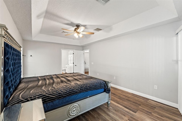 bedroom featuring dark hardwood / wood-style floors, connected bathroom, ceiling fan, a tray ceiling, and a textured ceiling