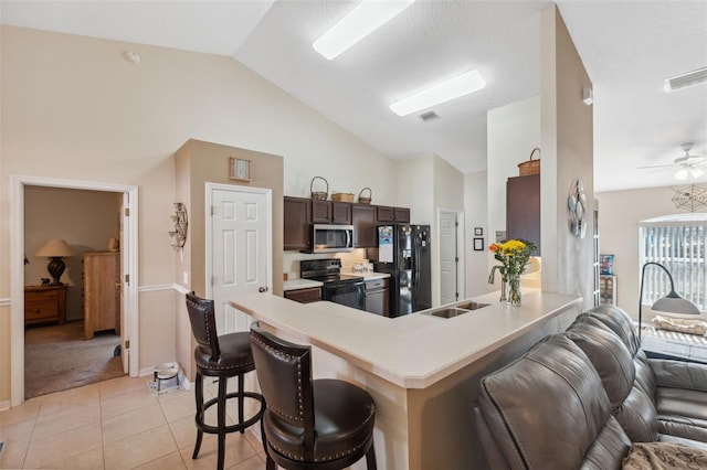 kitchen featuring dark brown cabinetry, sink, a kitchen breakfast bar, kitchen peninsula, and black appliances