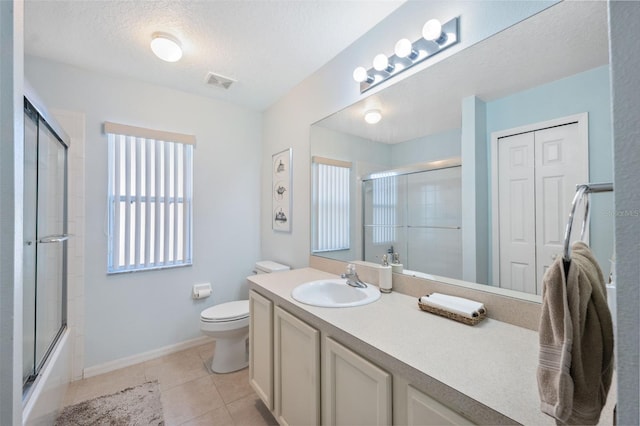 full bathroom with tile patterned flooring, bath / shower combo with glass door, vanity, a textured ceiling, and toilet