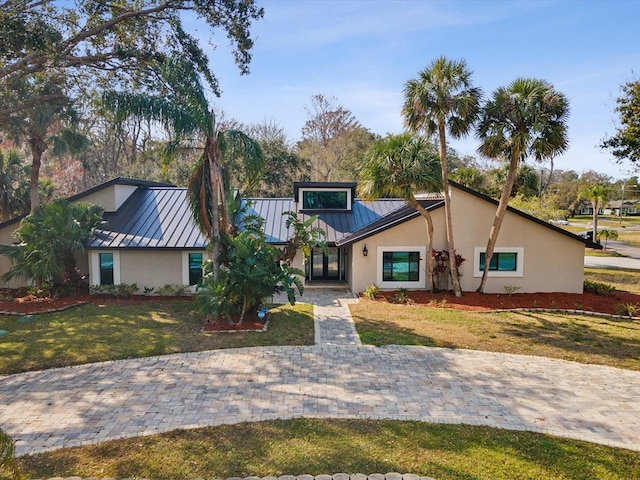 view of front of house with a standing seam roof, stucco siding, metal roof, and a front yard