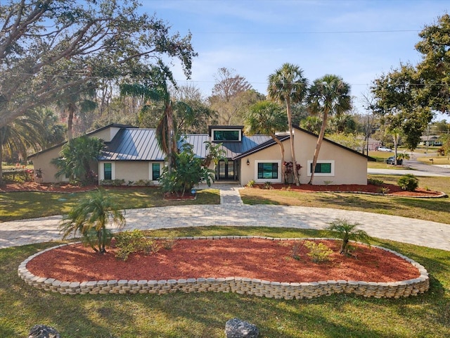 view of front of home featuring a front lawn, a standing seam roof, stucco siding, and decorative driveway