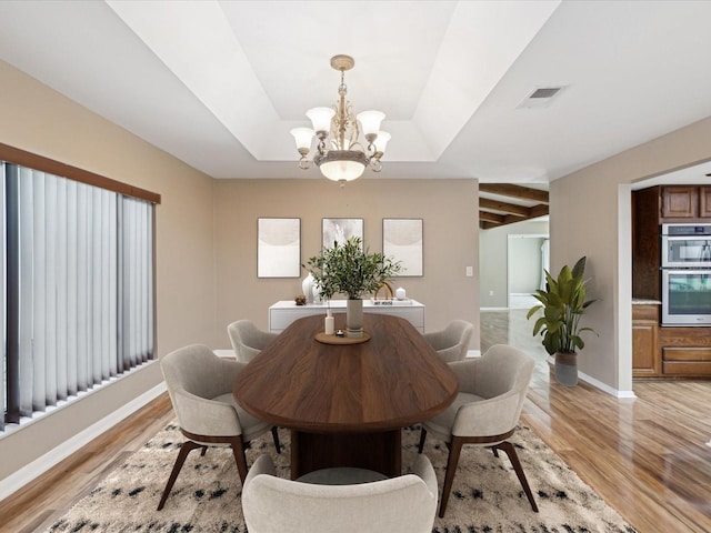 dining space with visible vents, baseboards, a raised ceiling, light wood-style flooring, and a chandelier