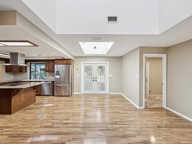 kitchen with a skylight, island range hood, appliances with stainless steel finishes, french doors, and light wood-style floors