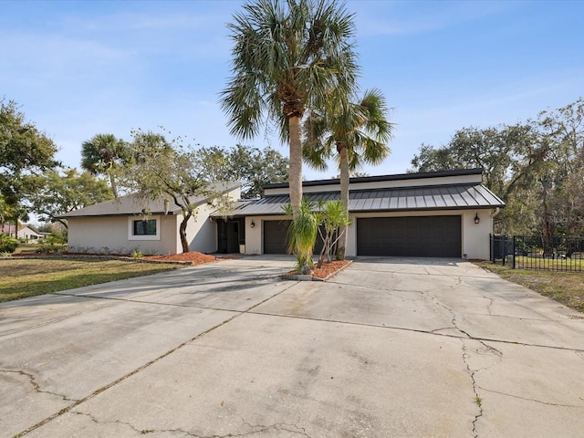 view of front of home featuring metal roof, a garage, fence, concrete driveway, and a standing seam roof