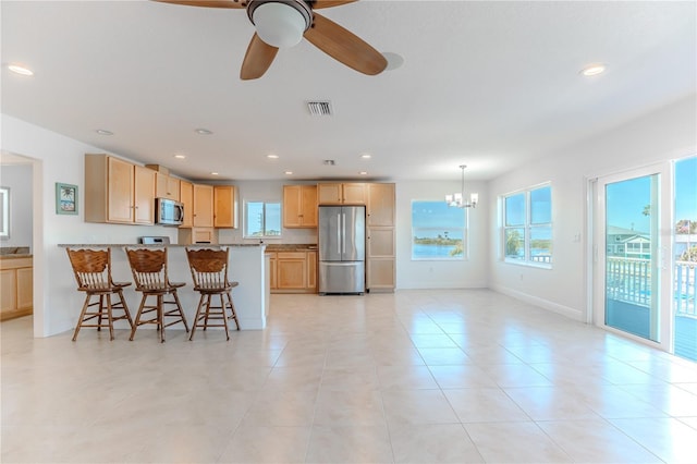 kitchen featuring appliances with stainless steel finishes, light stone counters, a kitchen bar, light brown cabinetry, and ceiling fan with notable chandelier