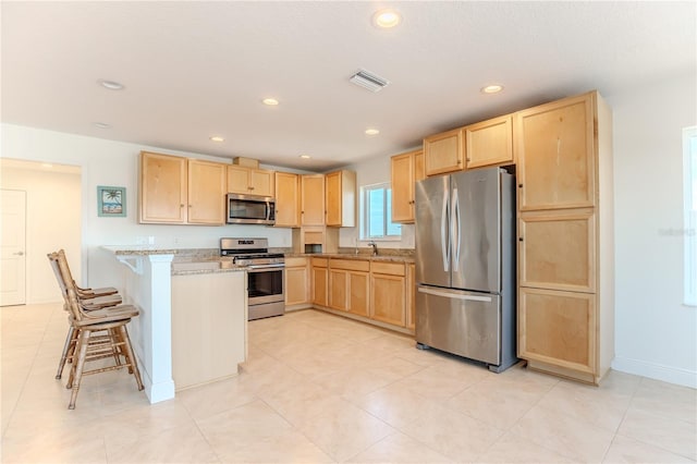 kitchen with sink, a breakfast bar area, light brown cabinets, appliances with stainless steel finishes, and light stone countertops