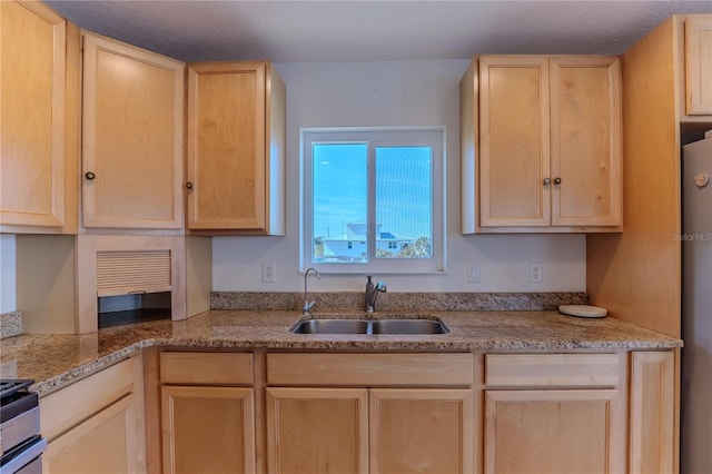 kitchen with stainless steel refrigerator, sink, light stone counters, and light brown cabinetry