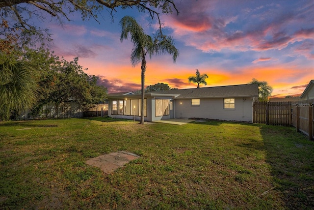 back house at dusk featuring a lawn and a patio