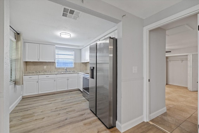 kitchen with stainless steel appliances, light stone countertops, white cabinets, and light hardwood / wood-style floors