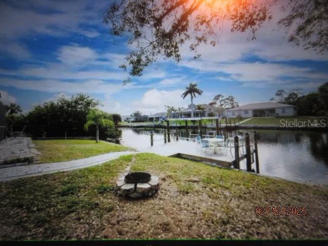 view of dock featuring a water view, an outdoor fire pit, and a lawn