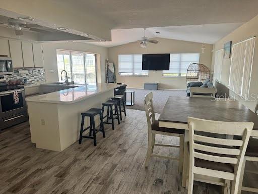 kitchen featuring stainless steel appliances, dark hardwood / wood-style floors, a kitchen breakfast bar, white cabinets, and vaulted ceiling