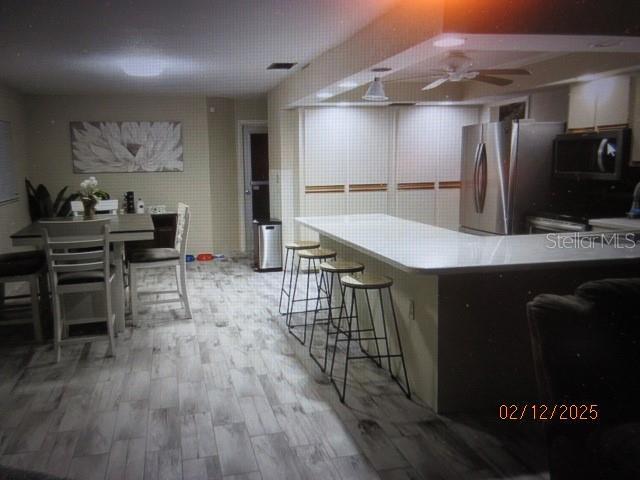 kitchen featuring a kitchen bar, stainless steel fridge, stove, and light wood-type flooring