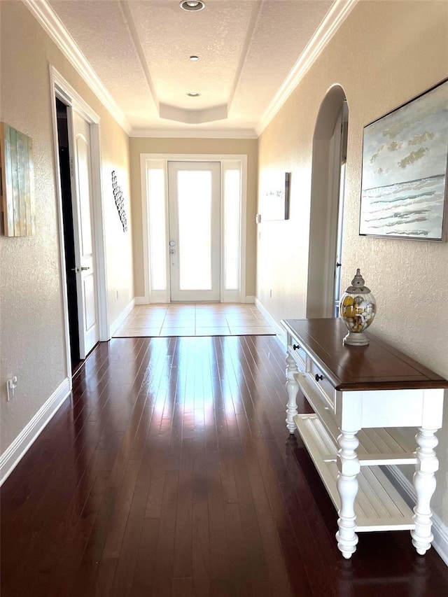 doorway to outside featuring ornamental molding, a tray ceiling, dark hardwood / wood-style flooring, and a textured ceiling