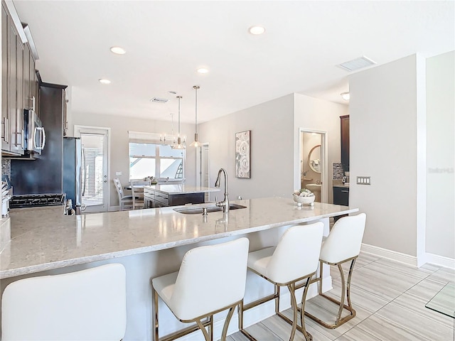 kitchen with sink, decorative light fixtures, appliances with stainless steel finishes, kitchen peninsula, and light stone countertops