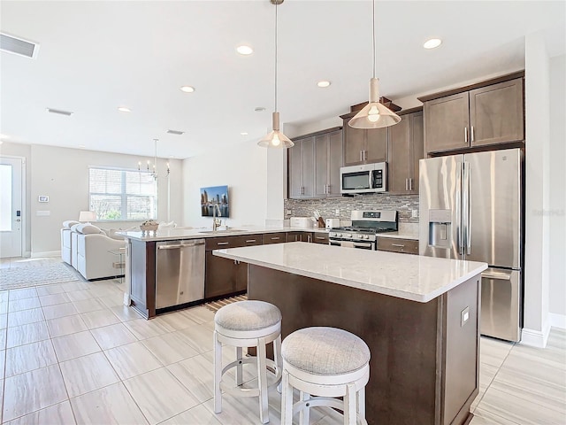 kitchen with tasteful backsplash, decorative light fixtures, kitchen peninsula, and appliances with stainless steel finishes