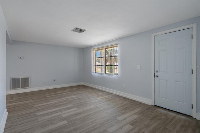 spare room featuring wood finished floors, visible vents, and baseboards