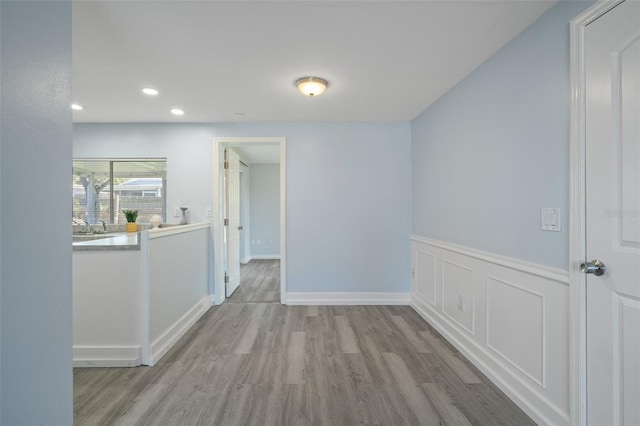 spare room with recessed lighting, a wainscoted wall, a sink, wood finished floors, and baseboards