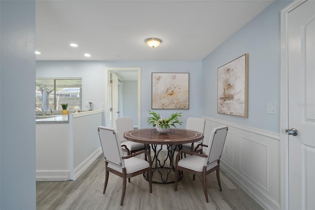 dining area with light wood-type flooring, recessed lighting, a decorative wall, and wainscoting