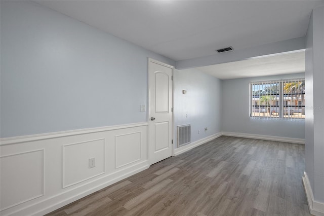 empty room with visible vents, a decorative wall, wood finished floors, and wainscoting