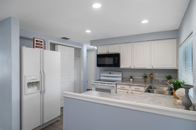 kitchen featuring a peninsula, white appliances, a sink, visible vents, and white cabinets