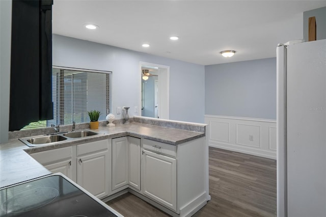 kitchen featuring dark wood-style floors, a wainscoted wall, freestanding refrigerator, white cabinetry, and a sink