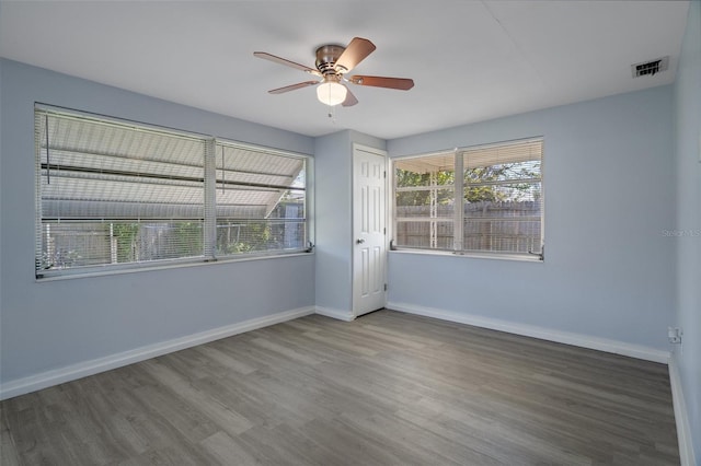 spare room featuring plenty of natural light, wood finished floors, visible vents, and baseboards