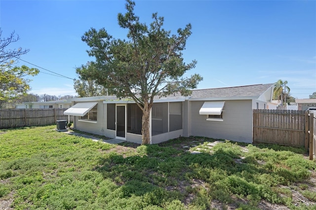 rear view of property featuring a sunroom, a fenced backyard, central AC unit, and a lawn