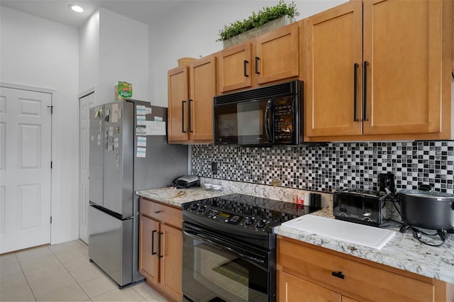 kitchen featuring backsplash, light stone countertops, light tile patterned flooring, and black appliances