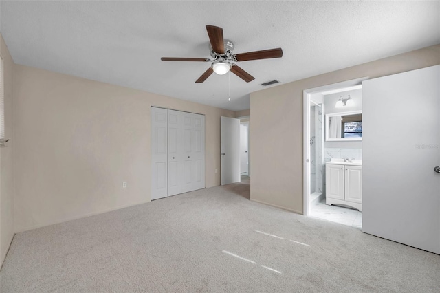 unfurnished bedroom with ensuite bathroom, ceiling fan, light carpet, a textured ceiling, and a closet