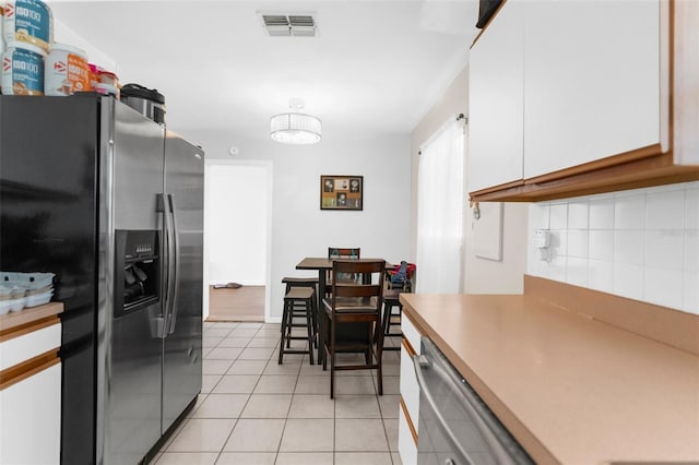 kitchen with light tile patterned floors, white cabinets, backsplash, and stainless steel fridge with ice dispenser