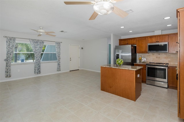 kitchen featuring a center island, ceiling fan, stainless steel appliances, light stone countertops, and decorative backsplash