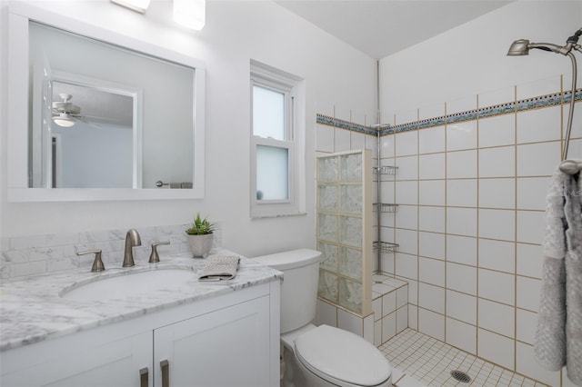 bathroom with vanity, ceiling fan, toilet, and tiled shower