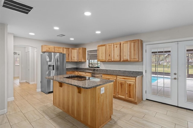 kitchen with french doors, a breakfast bar area, a center island, dark stone countertops, and appliances with stainless steel finishes