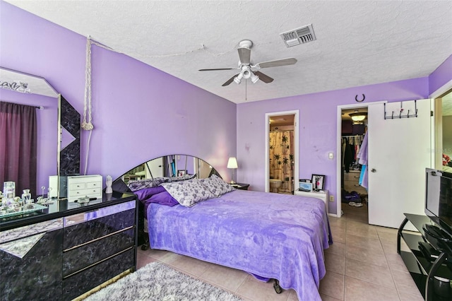 bedroom featuring ensuite bathroom, a textured ceiling, light tile patterned flooring, a walk in closet, and a closet