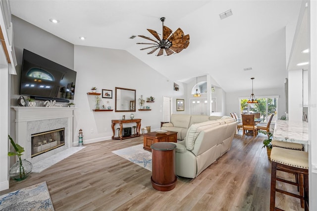 living room featuring a premium fireplace, lofted ceiling, ceiling fan, and light hardwood / wood-style flooring