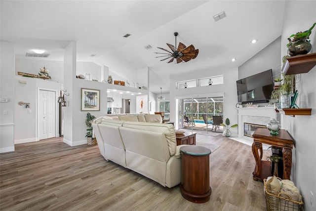 living room featuring ceiling fan, a high end fireplace, high vaulted ceiling, and light hardwood / wood-style floors