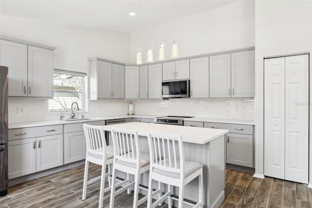 kitchen with sink, gray cabinets, a kitchen island, stainless steel appliances, and a kitchen bar