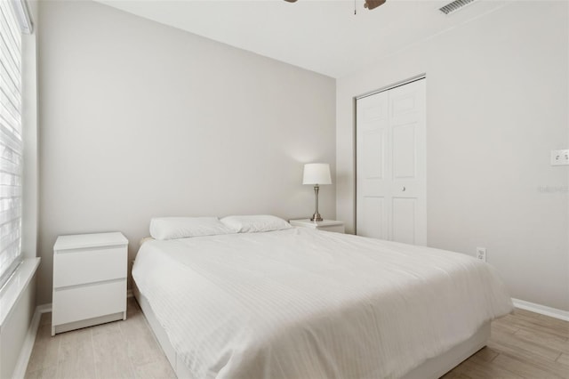 bedroom with multiple windows, ceiling fan, light wood-type flooring, and a closet