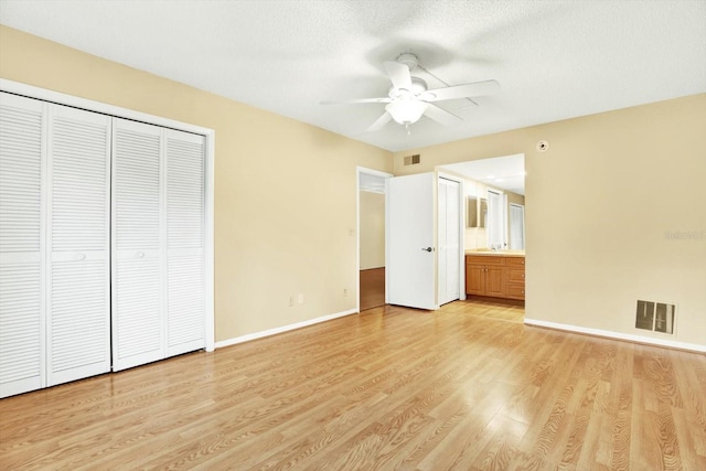 unfurnished bedroom with ensuite bathroom, ceiling fan, a textured ceiling, and light wood-type flooring