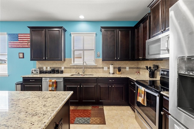 kitchen featuring stainless steel appliances, dark brown cabinetry, a sink, and light stone counters